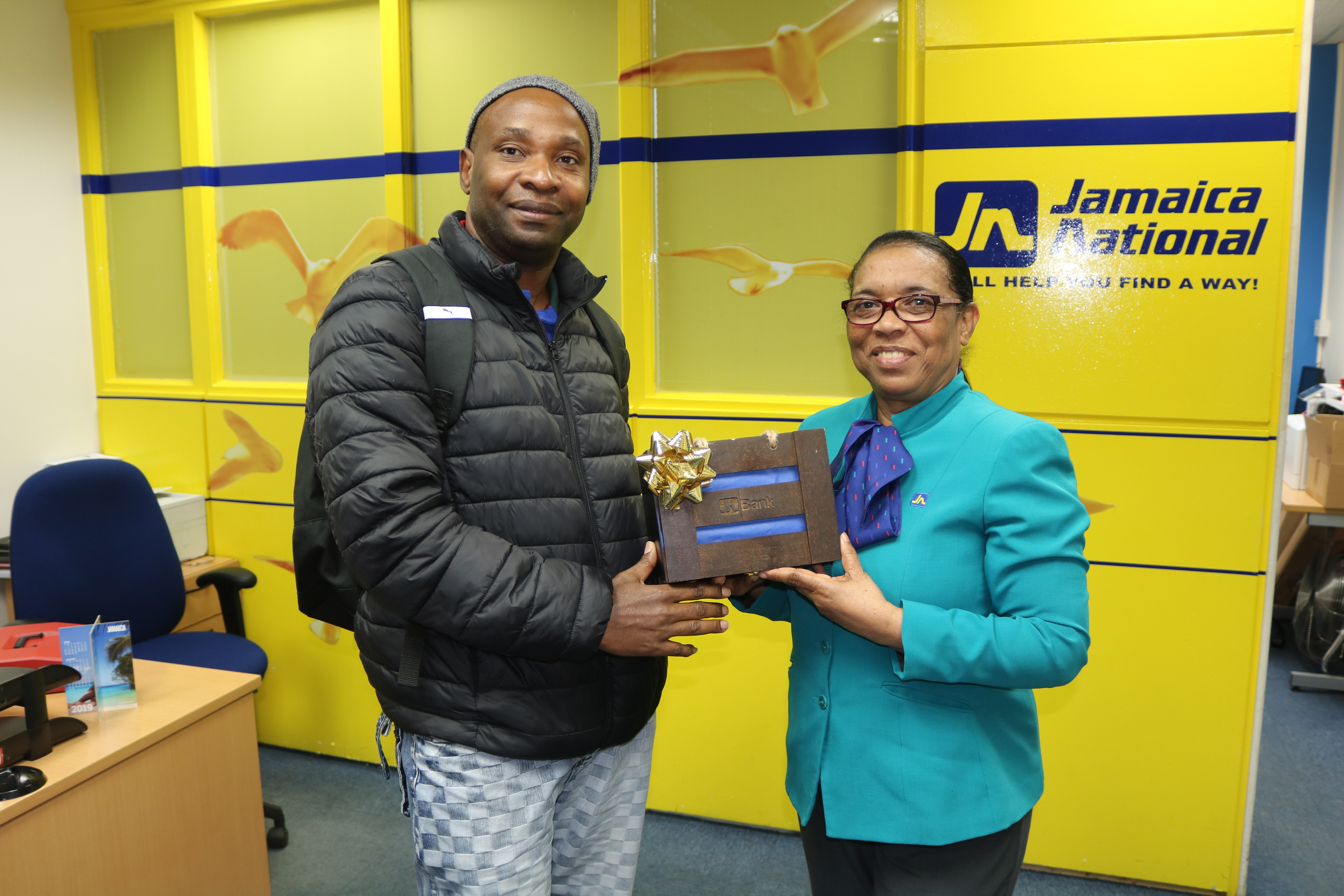 IMG_5252 - JN Bank Arnett Pryce (right), member service representative, JN Bank UK Representative Office presents Stanhope Gibbs, a JN member with a “Braata box” as part of the organisation’s “Celebrate our Jamaican Heritage Promotion”. Mr Gibbs received an authentic token that was made by a social enterprise in Jamaica for opening a JN Bank Savings Account .